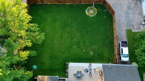 An aerial view of a fenced backyard with a lawn, a patio area with seating, and a vehicle parked on the street. - Hometown Haven
quiet•peaceful•cozy (Hancock)