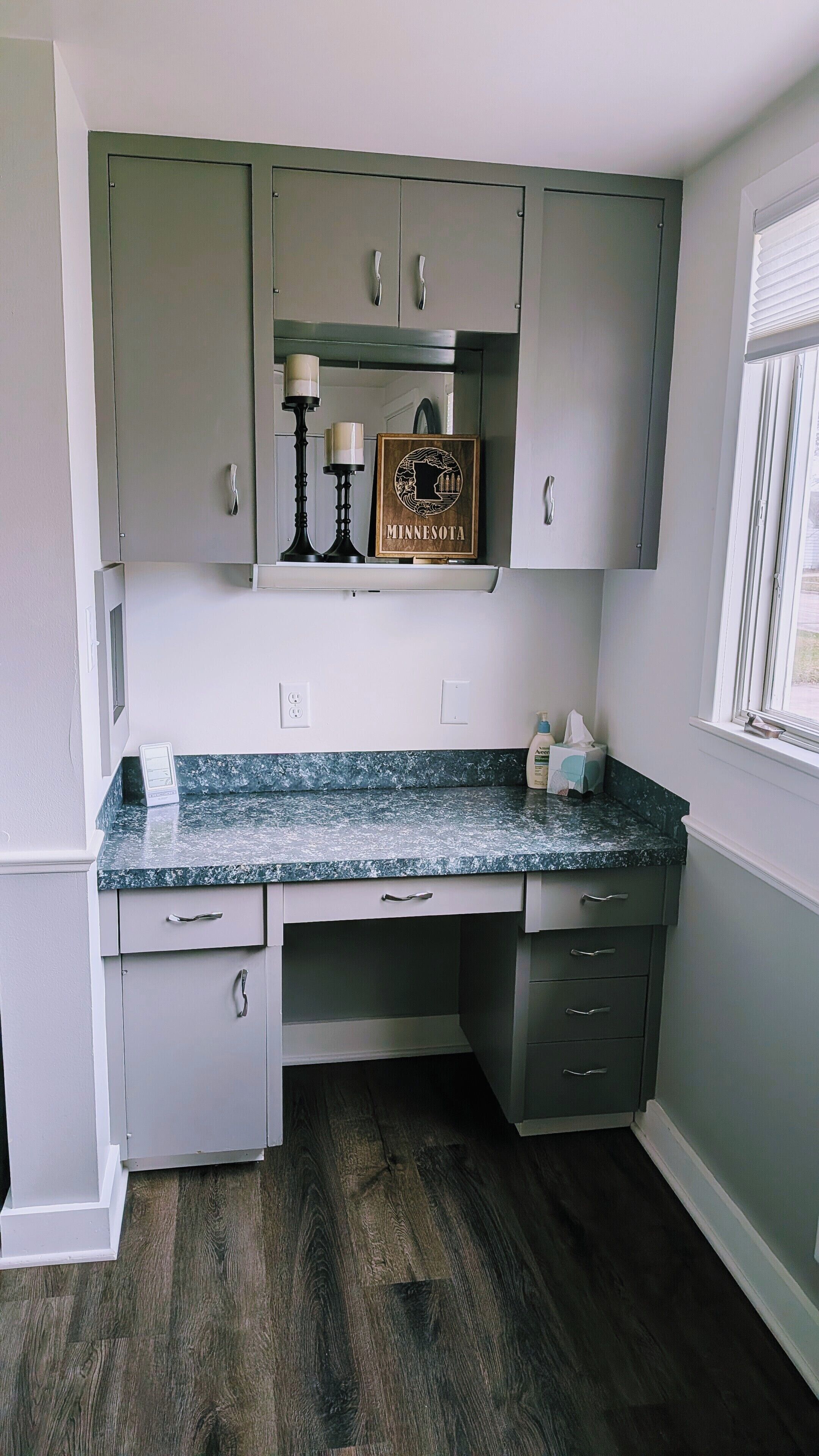 A kitchen with grey cabinets, a granite countertop, and a wooden sign with 'MINNESOTA' on it.