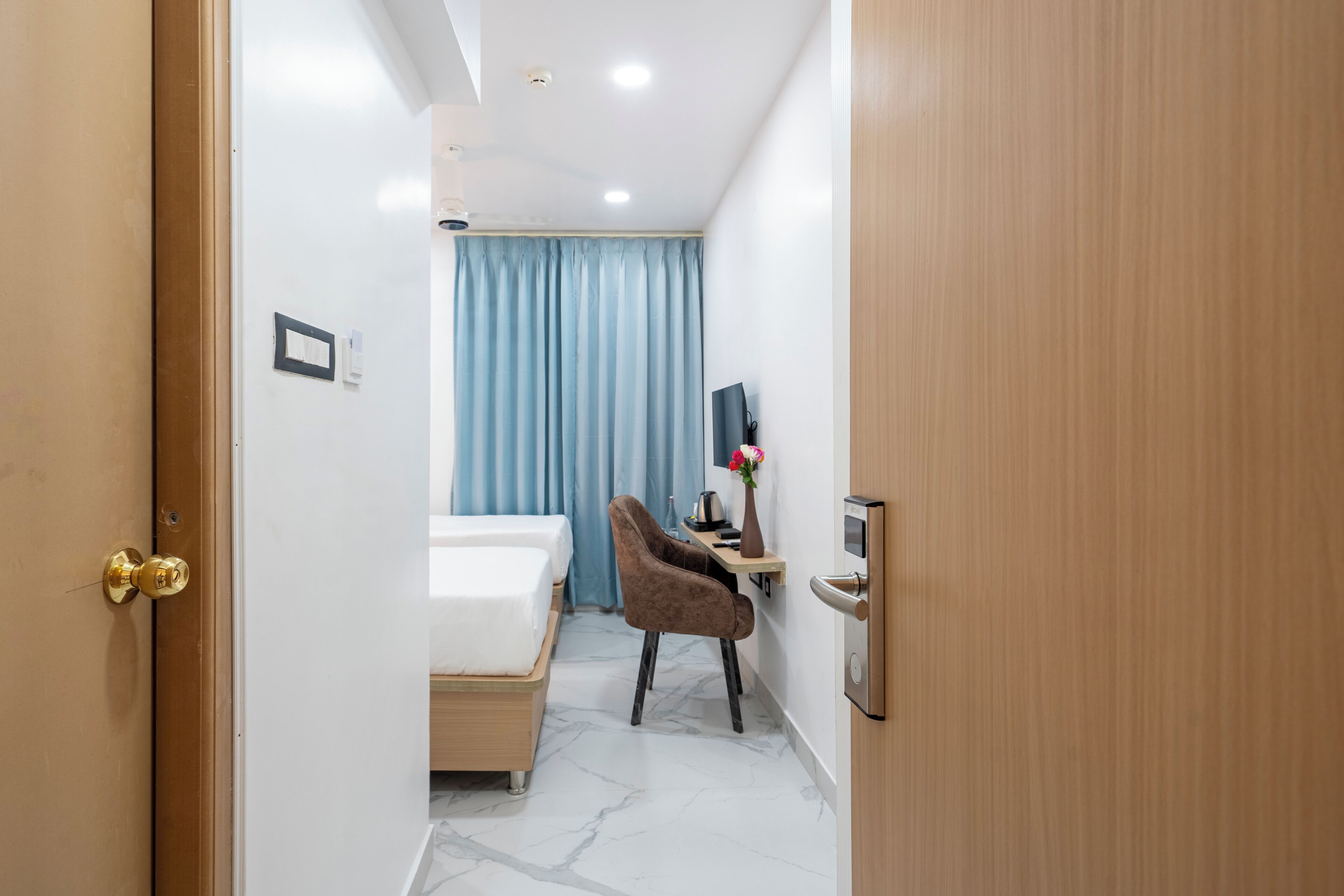 A hotel room with a bed, a desk with a computer, a chair, a TV, and a window with curtains.