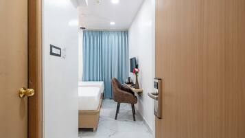 Habitación de hotel con cama, escritorio con computadora, silla, televisor y ventana con cortinas.