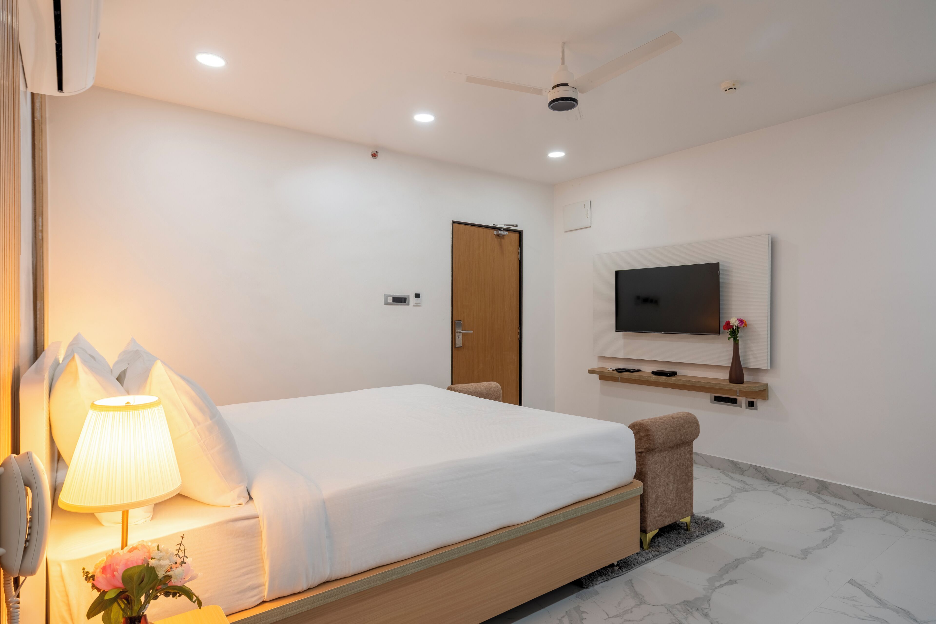 Una habitación de hotel moderna con una cama individual, una lámpara de noche, un televisor de pantalla plana montado en la pared y un ventilador de techo.