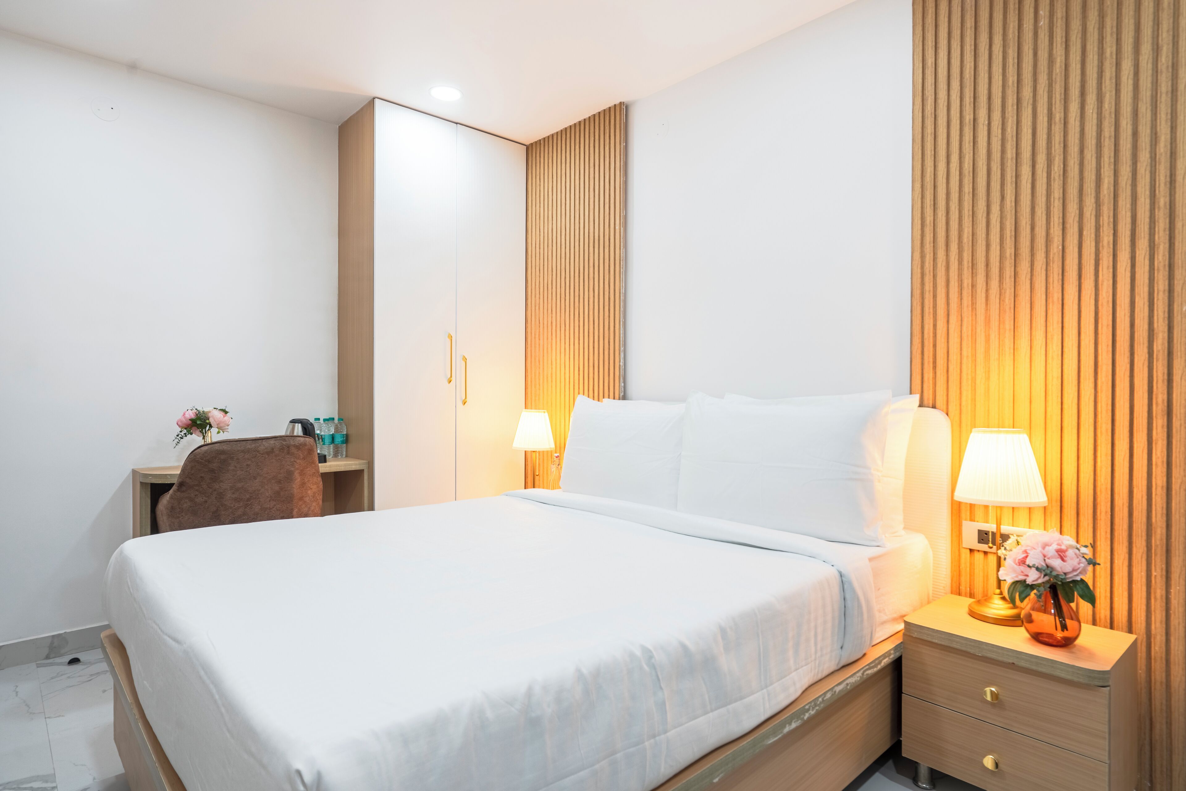 Habitación de hotel con una cama grande, lámparas de noche, un escritorio con silla y un panel de pared de madera.