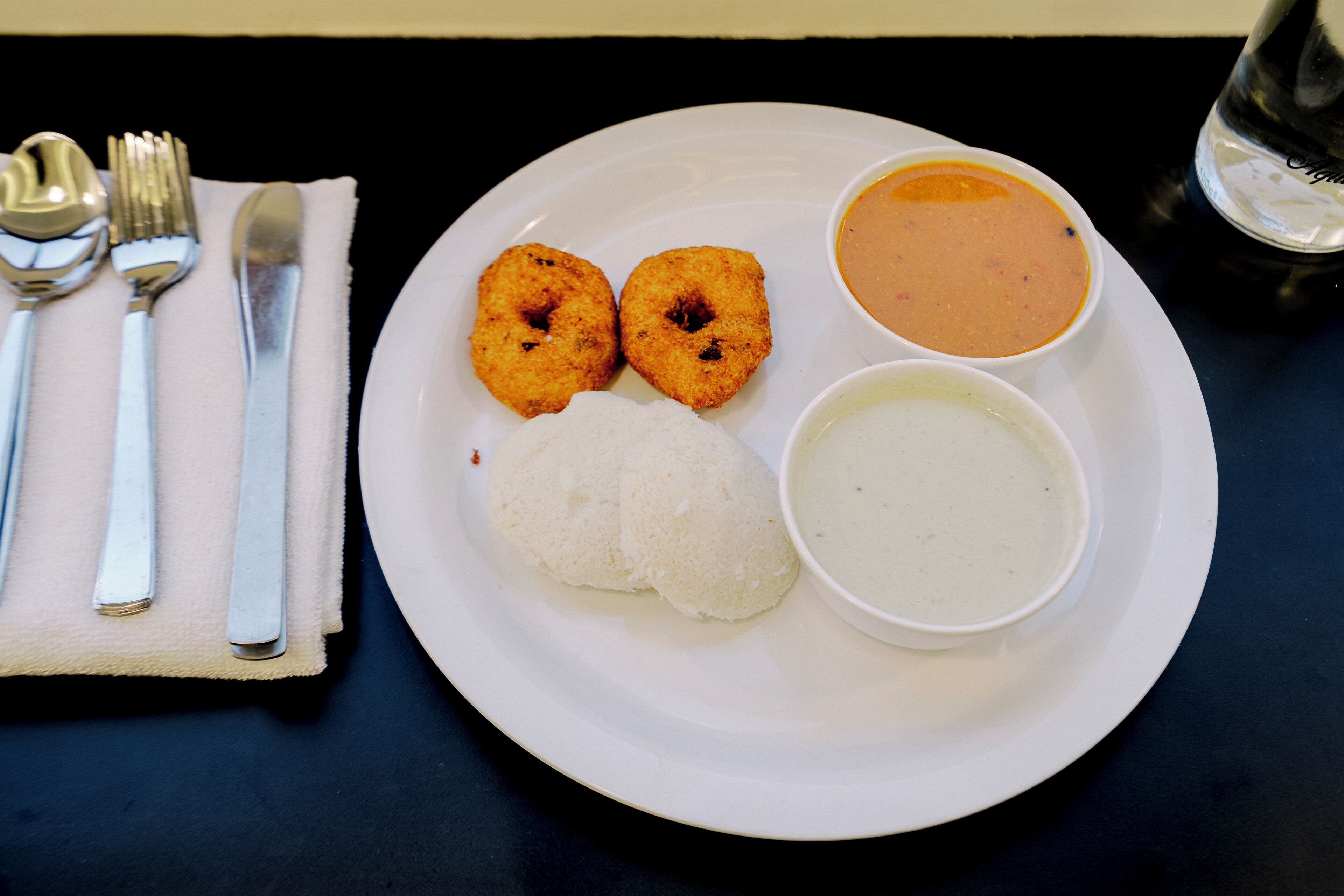 A white plate with two fried items, a mound of rice, and two bowls of soup on a dark table.