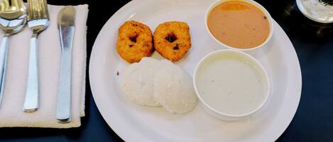 A white plate with two fried items, a mound of rice, and two bowls of soup on a dark table.