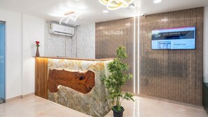 A reception desk with a marble top, a wooden accent, and a potted plant. A digital screen displays hotel information. - RCC Gachibowli (Hyderabad)