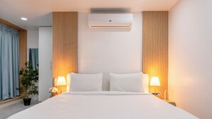 A hotel room with a large bed, two bedside lamps, an air conditioning unit, and a potted plant. - RCC Gachibowli (Hyderabad)