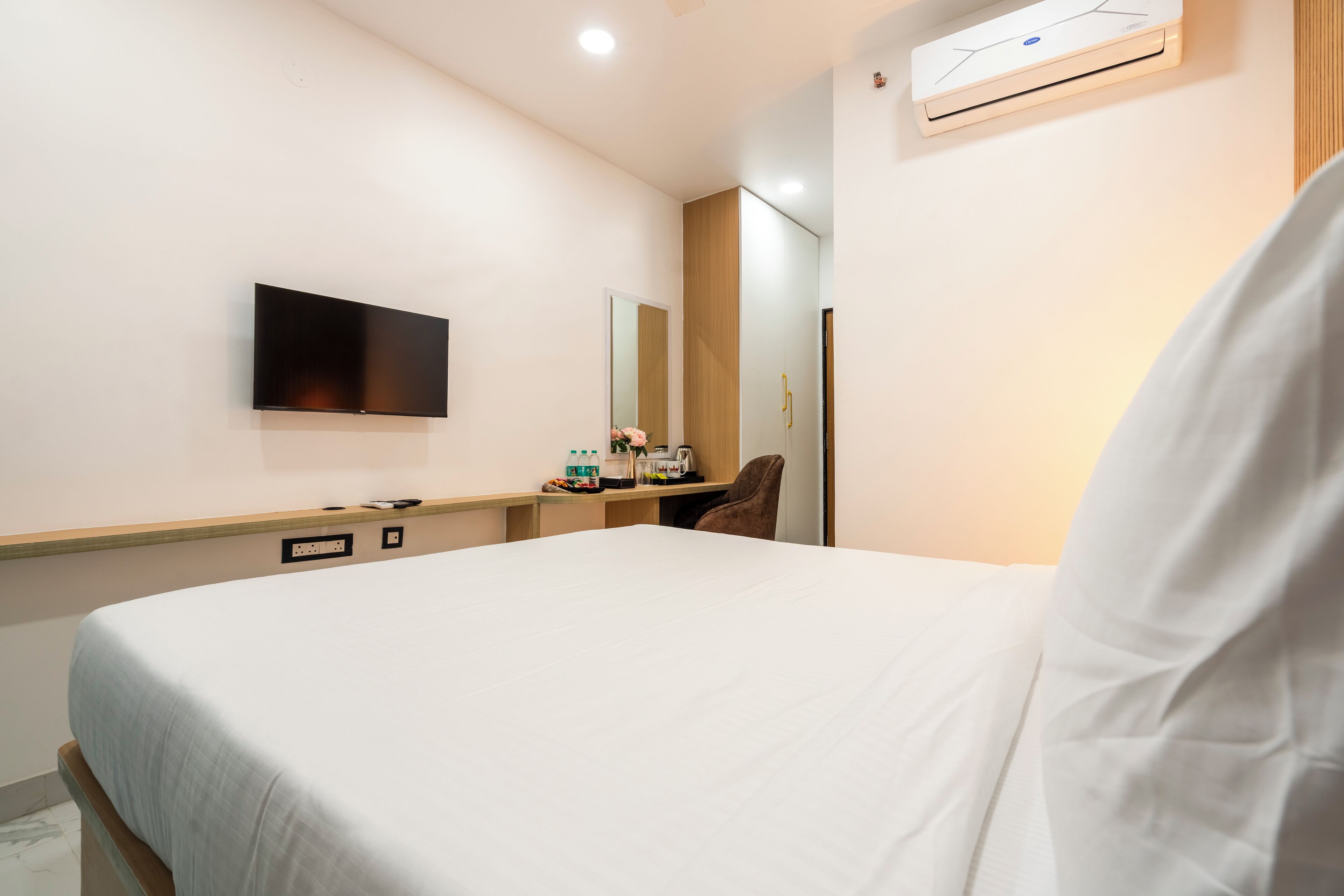 Ein Hotelzimmer mit Bett, Wandfernseher, Spiegel, Schreibtisch und Stuhl sowie einer Klimaanlage.