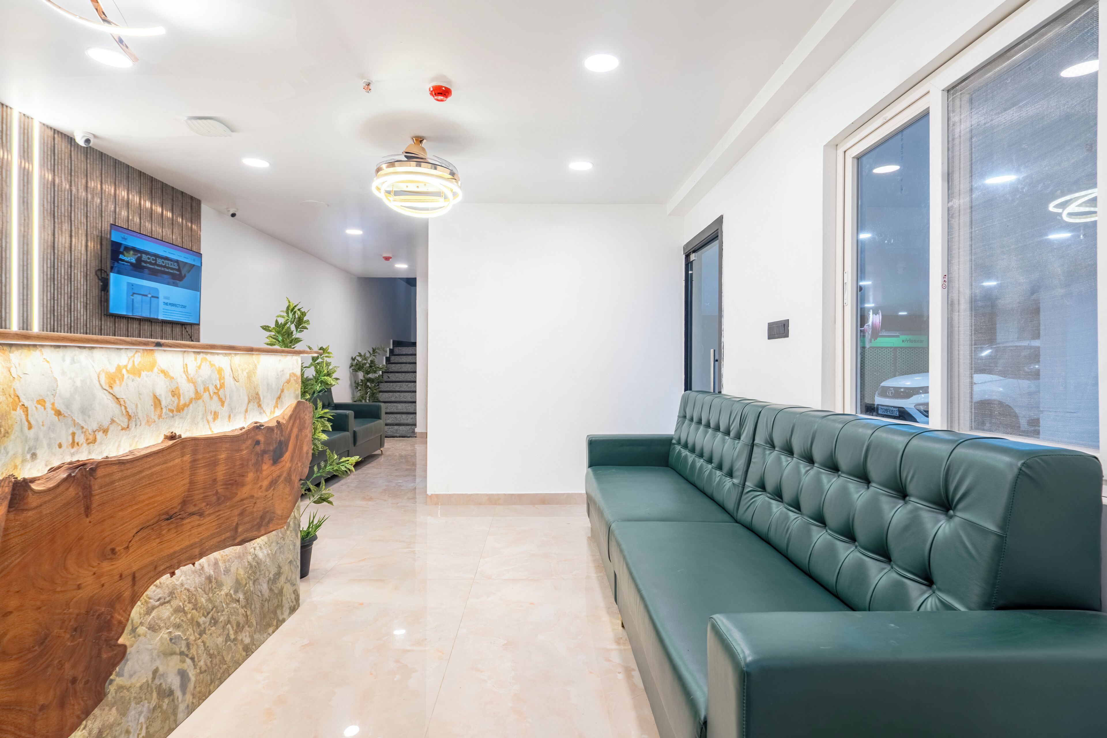 Un área de recepción con un mostrador de madera, un sofá verde y un amplio ventanal con vista a coches estacionados.