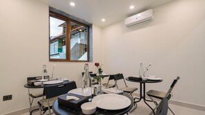 A dining area with a table set for two, a window with a view of a building, and an air conditioning unit on the wall. - RCC Gachibowli (Hyderabad)