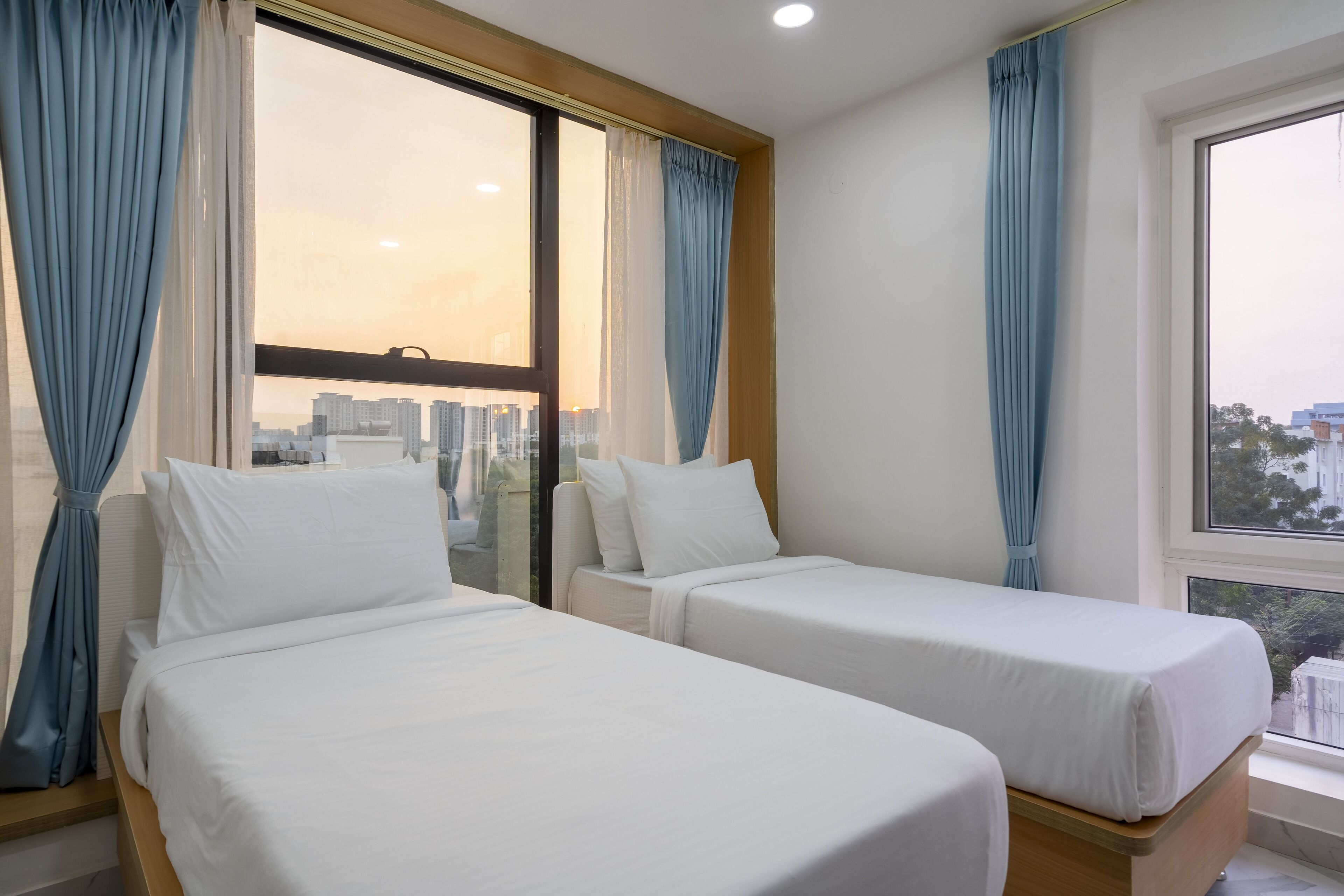 Quarto de hotel com duas camas de solteiro, uma janela grande com cortinas e vista para a cidade.