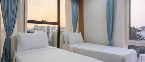 Quarto de hotel com duas camas de solteiro, uma janela grande com cortinas e vista para a cidade.