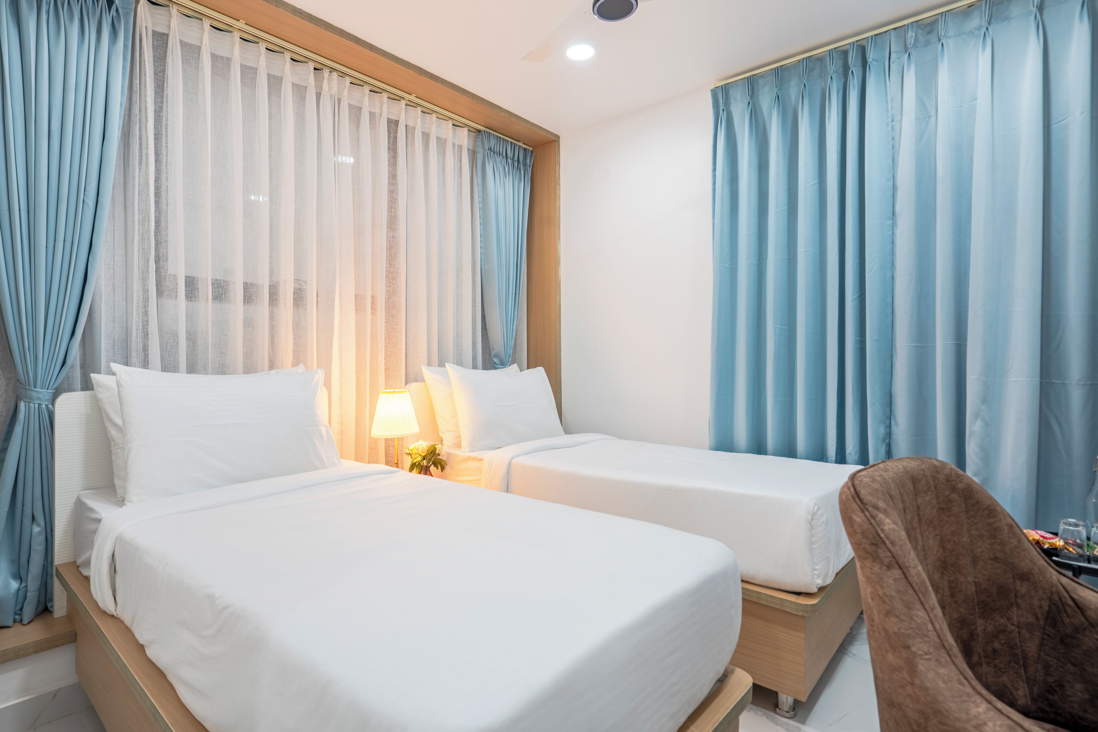 A hotel room with two beds, a brown chair, and a table with a lamp.