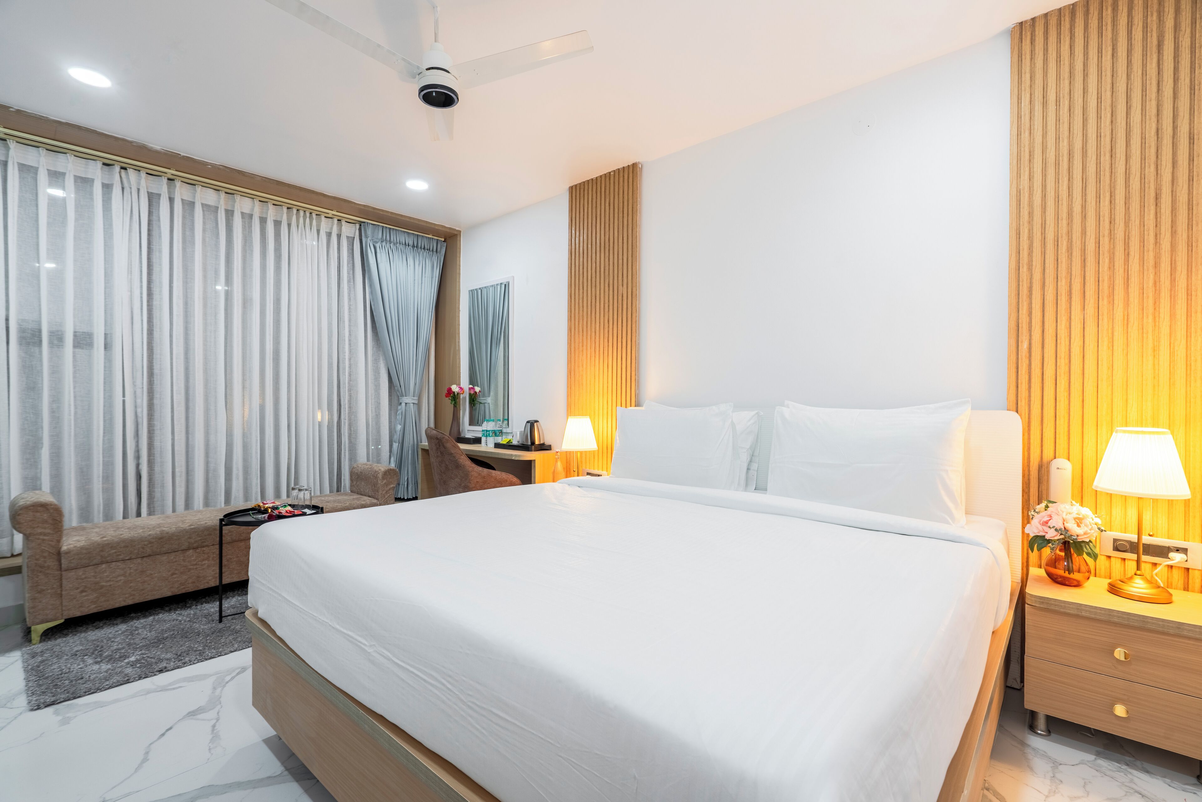 A hotel room with a large bed, a desk with a lamp, a chair, and a sofa.