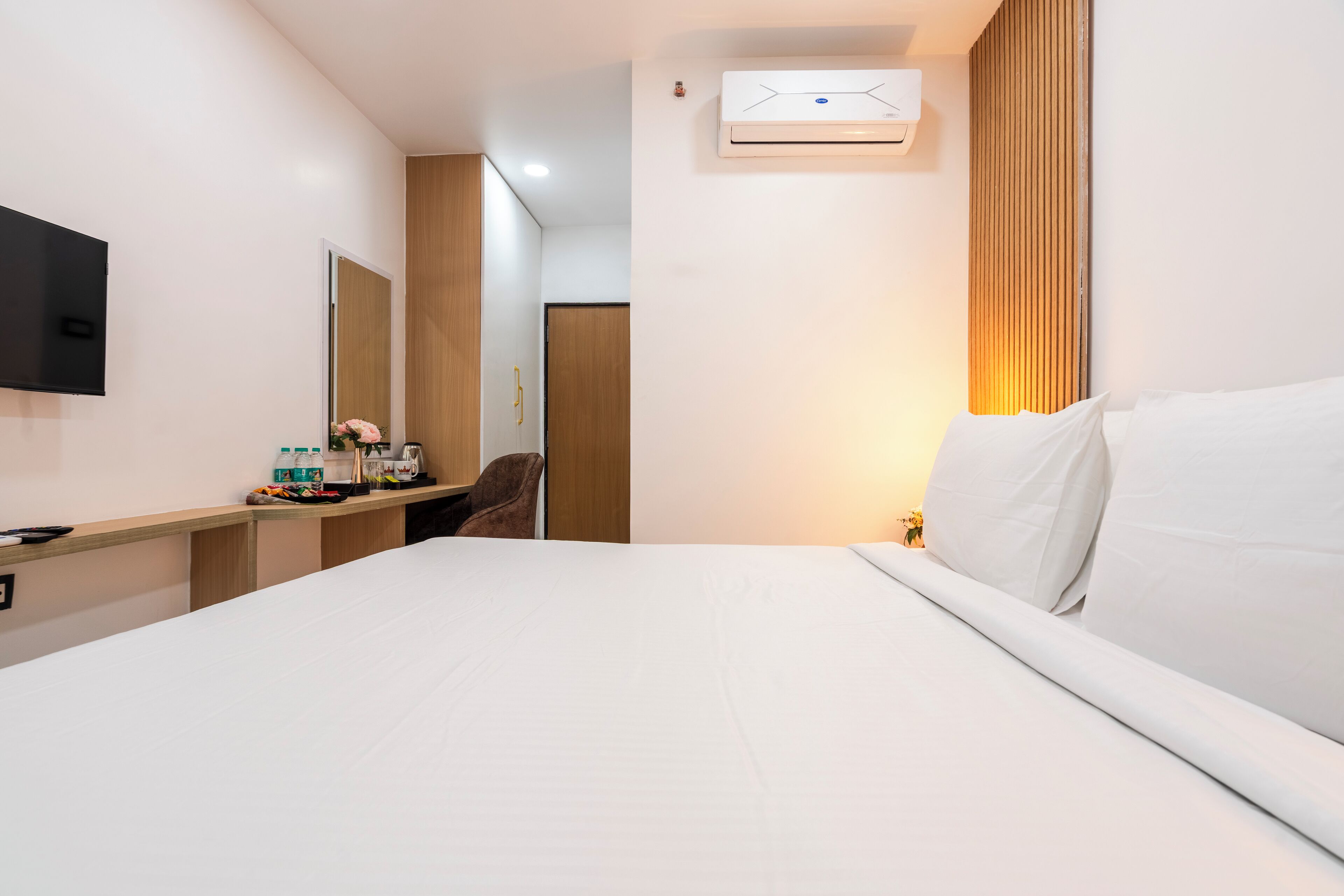 A hotel room with a bed, a desk, a chair, a TV, and an air conditioning unit.