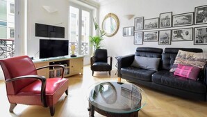 Uma sala de estar com um sofá de couro preto, uma poltrona de couro vermelha, uma mesa de centro de vidro e uma TV em um armário de madeira.