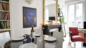 Uma sala de jantar com mesa de vidro posta para quatro pessoas, uma estante, um quadro e um espelho.