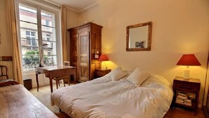 Quarto com cama grande, mobiliário de madeira, escrivaninha e janela com cortinas.
