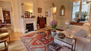 Uma sala de estar aconchegante com lareira, um sofá branco, uma mesa de centro e um tapete estampado.
