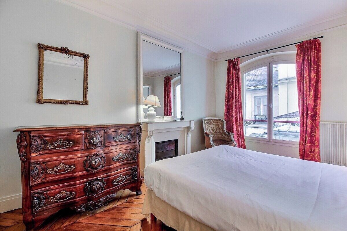 Ein Schlafzimmer mit einem hölzernen Schminktisch, einem Bett, einem Spiegel und einem Fenster mit Vorhängen.