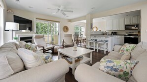 A spacious living room with a fireplace, a dining area, and a kitchen with white cabinets. - SUPER SPACIOUS TOWNHOUSE IN POOL CMMTY- 3101 The Palms, Rehoboth (Rehoboth Beach)