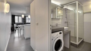 A modern bathroom with a glass shower enclosure, a built-in washing machine, and a vanity with a mirror. - Parisian Home | 2 chambres | Sentier - Bonne Nouvelle (Paris)