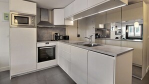 A modern kitchen with white cabinetry, a built-in microwave, a stove, and a sink. - Parisian Home | 2 chambres | Sentier - Bonne Nouvelle (Paris)