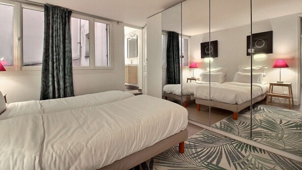 A hotel room with two beds, a large mirror, and a view of the street. - Parisian Home | 2 chambres | Sentier - Bonne Nouvelle (Paris)