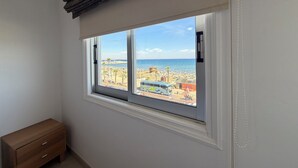 Una habitación con un ventanal grande que da a una playa, un banco de madera y una pared blanca.