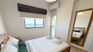 Un dormitorio con cama, ventana con vista al mar, aire acondicionado y espejo.