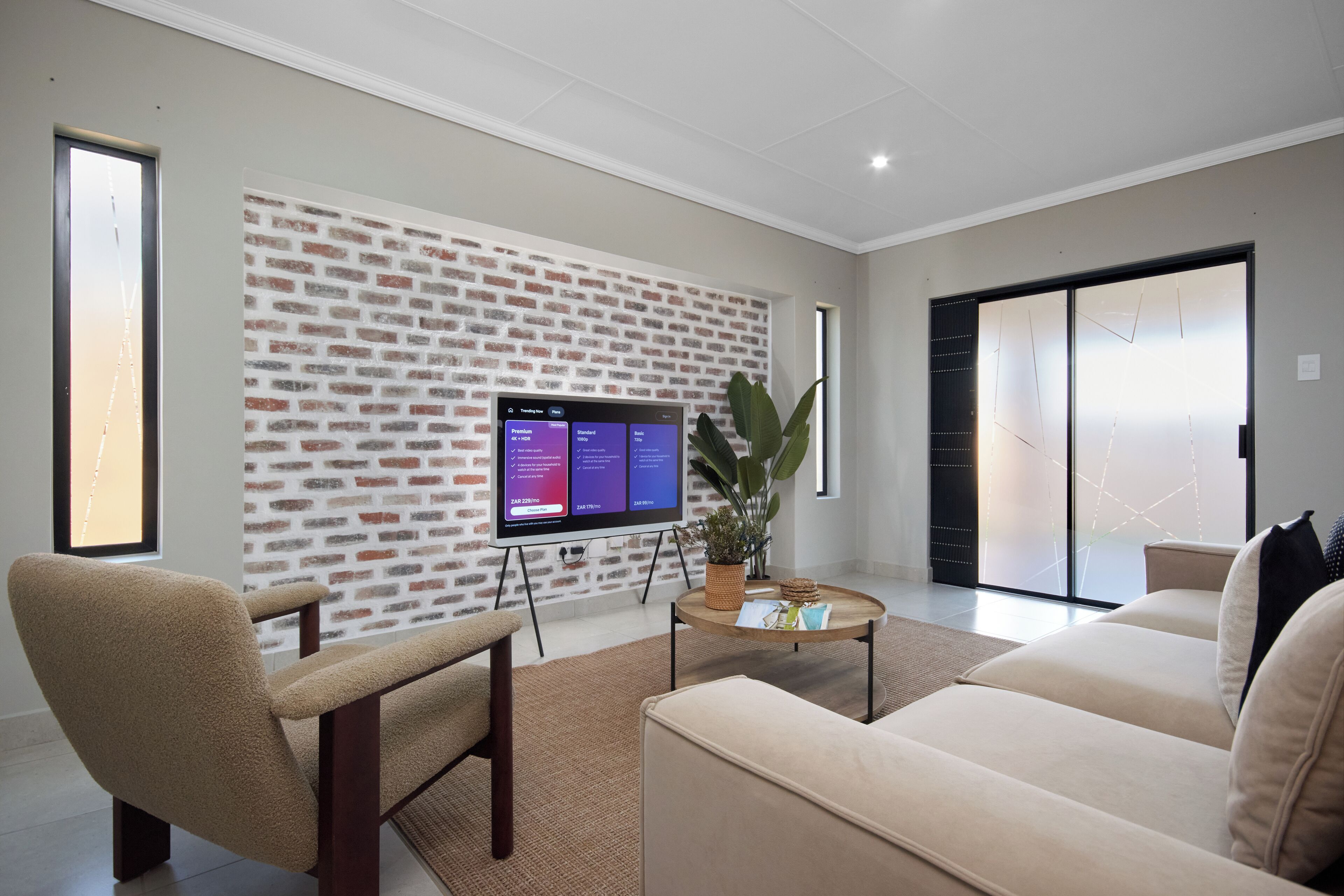 A modern living room with a brick wall, a flat-screen TV, a sofa, a chair, and a coffee table.