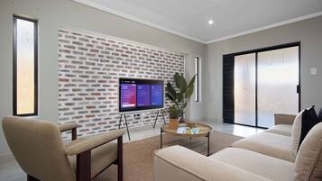 A modern living room with a brick wall, a flat-screen TV, a sofa, a chair, and a coffee table.