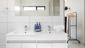 A modern bathroom with a large mirror, two sinks, and a shower.