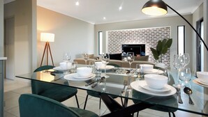 A modern dining area with a glass table set for four, surrounded by green upholstered chairs.