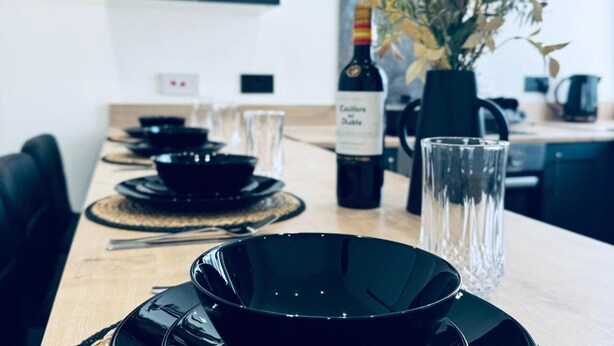 Una mesa de comedor con cuencos negros, una botella de vino y un florero con plantas secas.