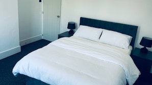 Una cama bien hecha con sábanas blancas, un cabecero oscuro y dos mesitas de noche con lámparas.
