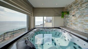 A modern bathroom with a large bathtub, a stone wall, and a view of the sea. - Mediterranean Luxury Stay with Sea Views & Jacuzzi (Xgħajra)