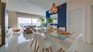 A modern dining area with a glass table, white chairs, and a hanging light fixture. - Mediterranean Luxury Stay with Sea Views & Jacuzzi (Xgħajra)