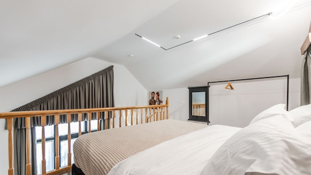 A bedroom with a large bed, a wooden staircase, a wardrobe, and a ceiling light fixture. - Muraga Villas 4 Xhubleta (Dajt)