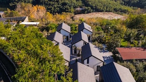 A residential area with modern houses featuring sloped roofs, surrounded by dense trees and a hilly backdrop. - Muraga Villas 4 Xhubleta (Dajt)