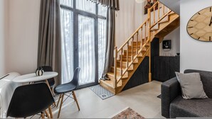 A modern living room with a staircase, a dining area with a table and chairs, and a large clock on the wall. - Muraga Villas 4 Xhubleta (Dajt)