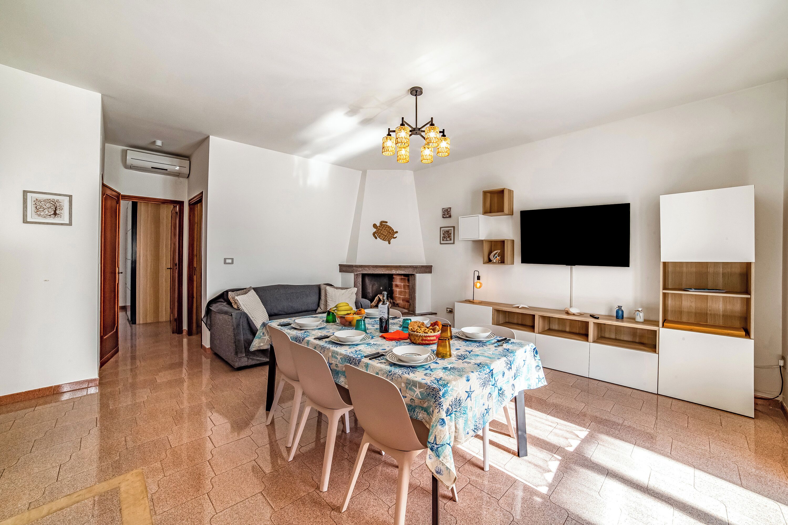 A dining area with a table set for four, a sofa, a fireplace, and a television mounted on the wall.