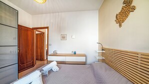 Quarto de hotel com cama, guarda-roupa de madeira, penteadeira com espelho e uma obra de arte na parede.