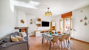 Uma sala de estar com um sofá, uma mesa de jantar posta para quatro pessoas e uma televisão na parede.