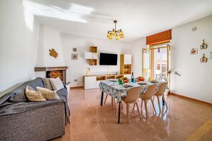 Ein Wohnzimmer mit einer Couch, einem Esstisch für vier Personen und einem an der Wand befestigten Fernseher.