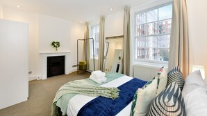 Habitación de hotel con cama, chimenea, ventana con cortinas y vistas a edificios.