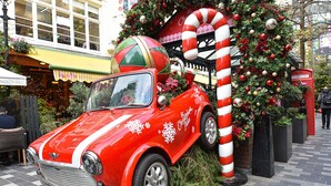 Un coche clásico rojo con decoraciones de copos de nieve aparcado frente a un árbol de Navidad y una decoración de bastón de caramelo.