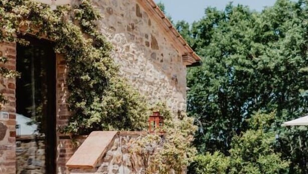 Un edificio in pietra con una scalinata che conduce a una porta, circondato da vegetazione e mobili da giardino.