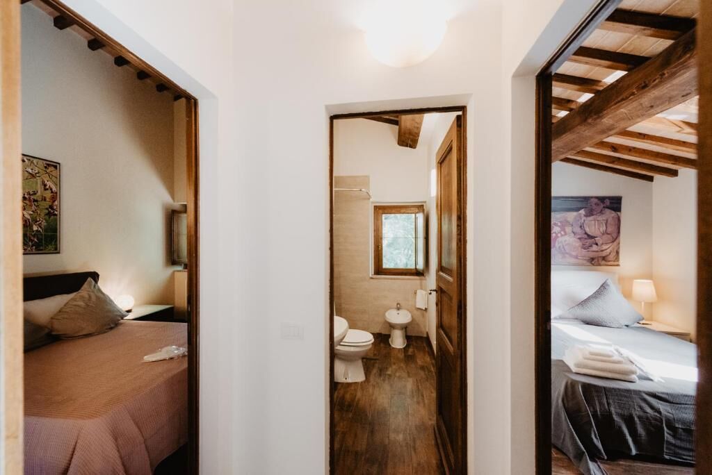 Een hotelkamer met een houten plafond, een bed met een blauwe deken, een nachtkastje met een lamp en uitzicht op de badkamer.