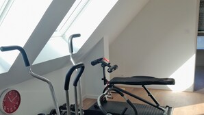 Un gimnàs a casa amb equip d'exercici, un rellotge i finestres veles.