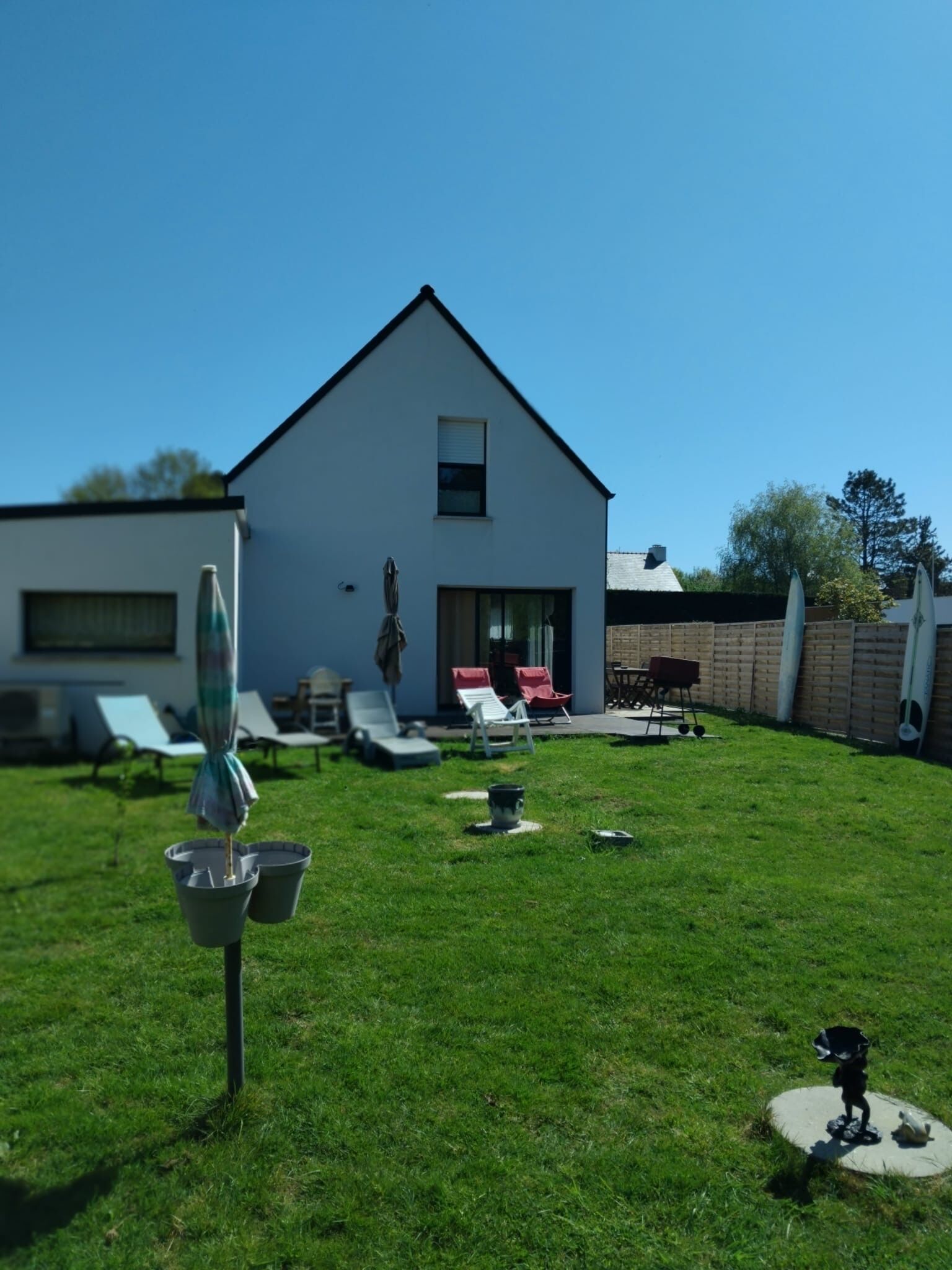 A modern house with a white exterior, a well-maintained lawn, and outdoor seating.